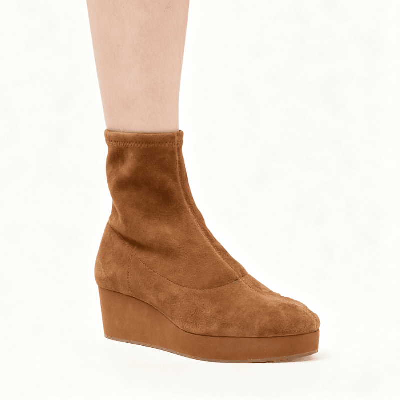 A single brown suede ankle boot with a wedge heel, shown on a model's foot against a plain white background.