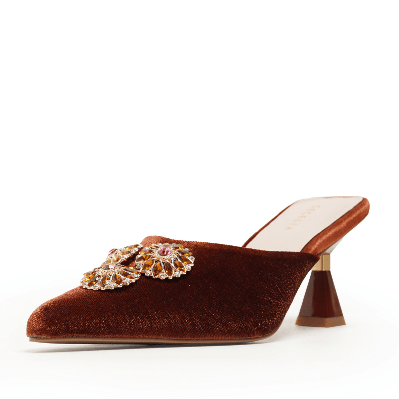 A single women's mule shoe in rich burgundy velvet, featuring a pointed toe adorned with a large jeweled floral embellishment and a sculptural cone heel, photographed on a clean white background.