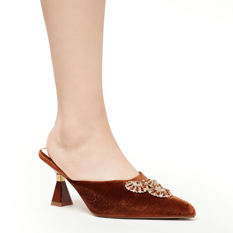 A single brown velvet mule high heel with a jeweled decorative embellishment on the toe, shown on a model's foot against a plain white background.