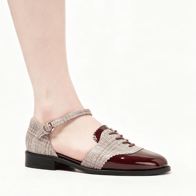 A woman's low-heeled Mary Jane flat shoe with a glossy burgundy patent toe cap, matching burgundy lace detail, and a textured beige tweed upper with an ankle strap and gold buckle, shown on a model's foot against a white background.