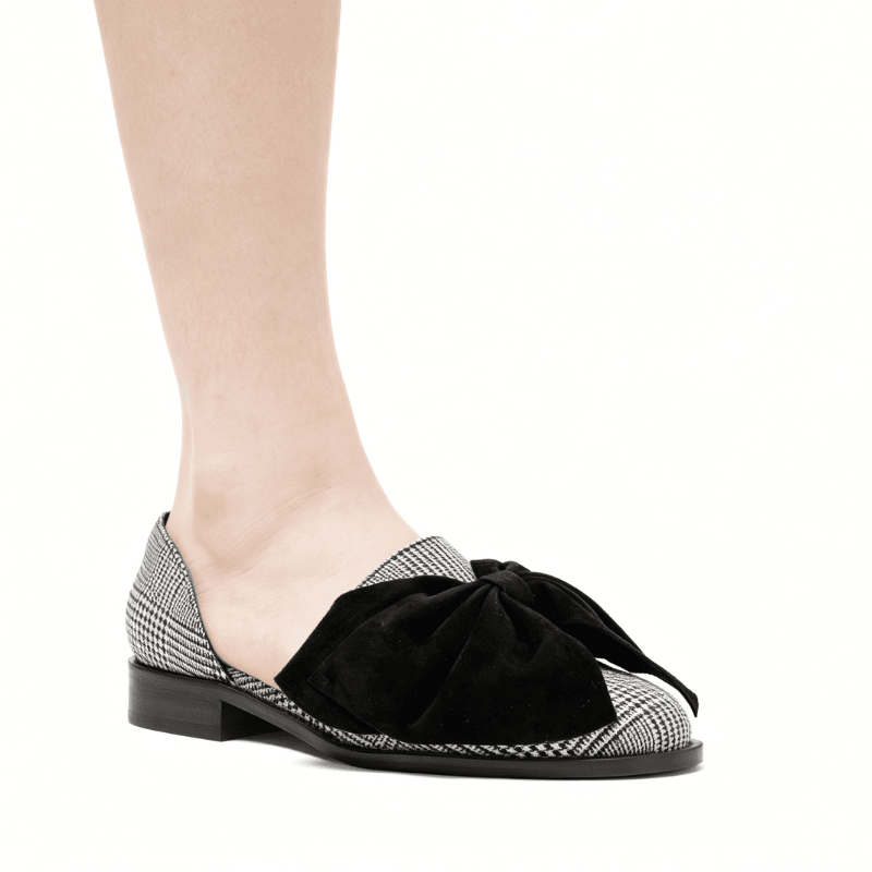 A black velvet bow loafer with a black and white houndstooth patterned toe cap and heel, shown on a model's foot against a white background.