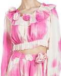 A woman wearing a pink and white watercolor print crop top with rosettes at the collar and a matching skirt.