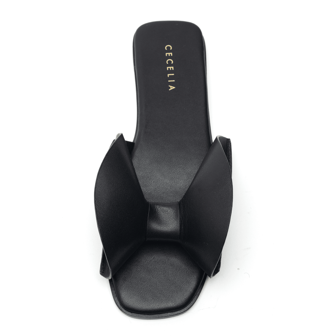 A black sandal with a voluminous bow on the vamp, set on a square toe and cushioned footbed, with the brand name 'CECILIA' visible on the heel.