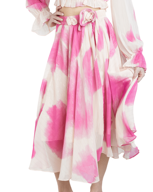 A midi length skirt with a flowy silhouette, featuring a soft ivory base with a delicate pink watercolor print and metallic strands, with an elastic waistband.